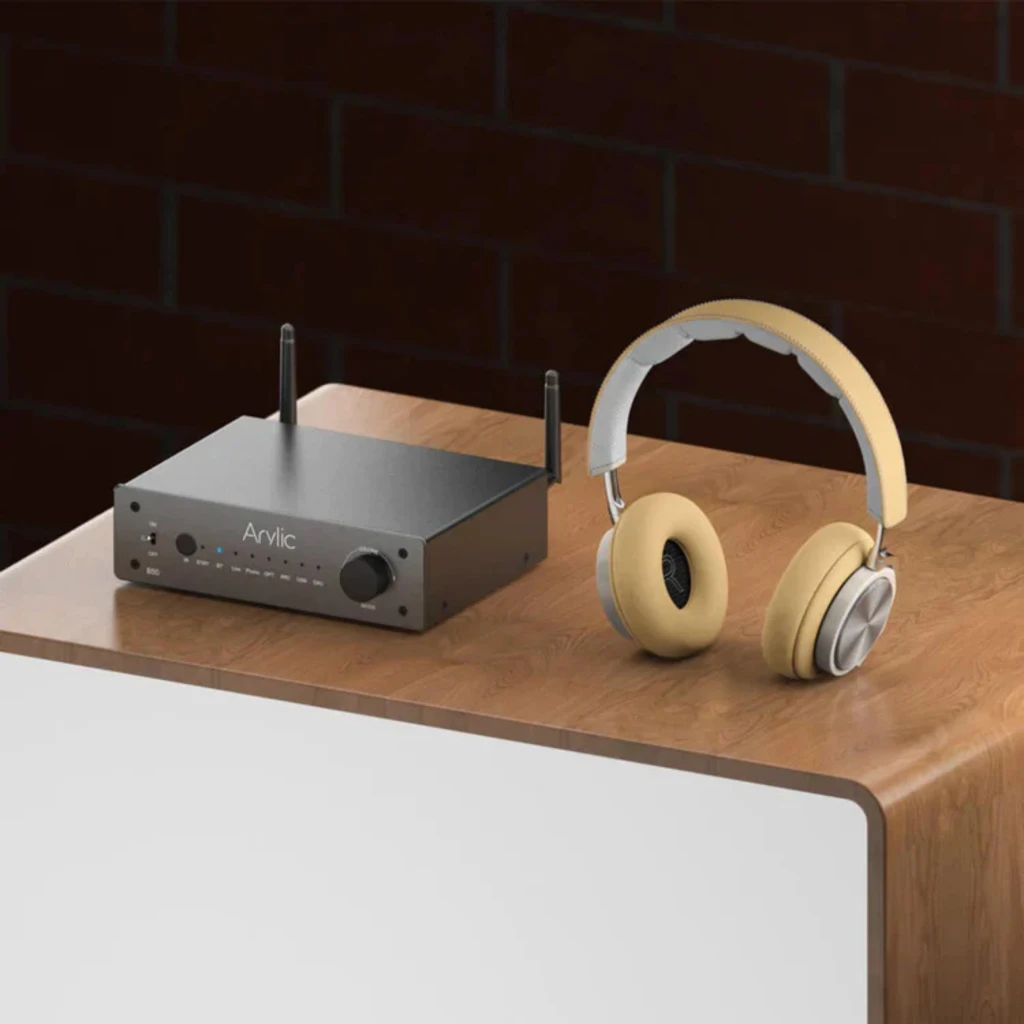 Arylic B50 Amplificador Bluetooth 5.2 Negro con antenas duales, chasis metálico mate, perilla frontal y LEDs indicadores; junto a audífonos beige over-ear