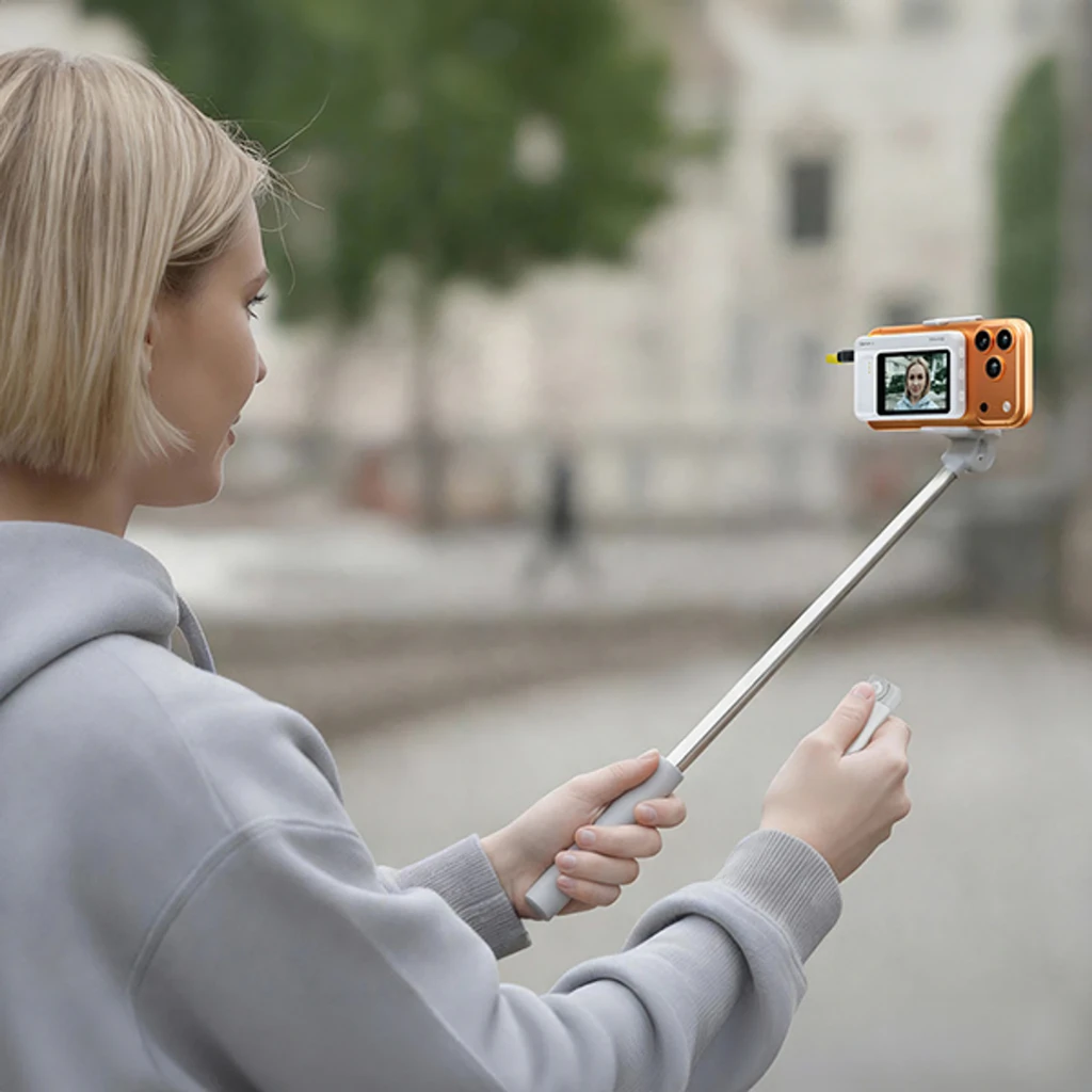 Monitor selfie 7RYMS Qshot V2 4K/60fps MagSafe + USB-C en uso con palo extensible, pantalla frontal mostrando retrato, acabado naranja con botones laterales