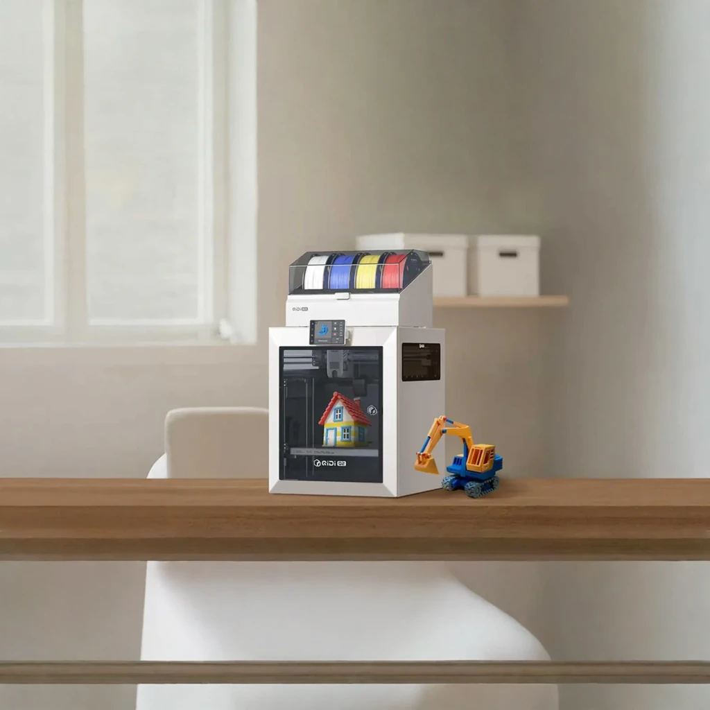 Impresora 3D Qidi Q2 FDM CoreXY compacta con carcasa blanca y ventana frontal, pantalla lateral y portabobinas superior multicolor; maqueta de casa impresa