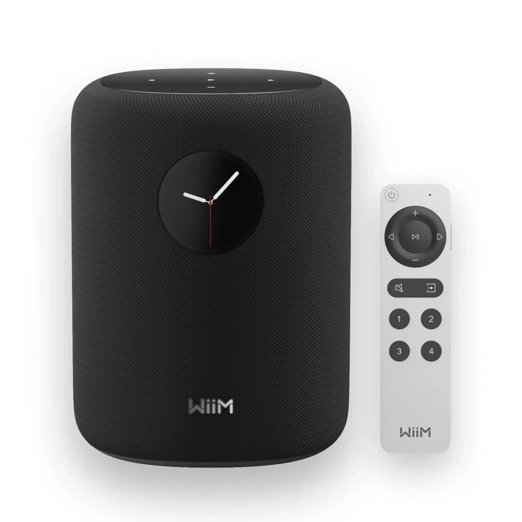 Wiim Sound negro, vista frontal con mando: altavoz negro con reloj analógico y mando a distancia blanco incluido