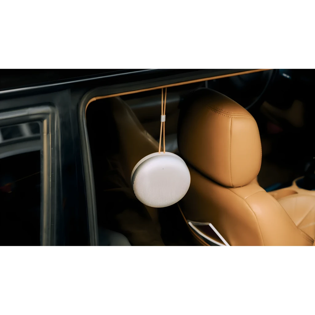Bang & Olufsen BeoSound A1 3rd Gen rojo, uso lifestyle: colgado con correa en ventanilla de coche con asiento de cuero