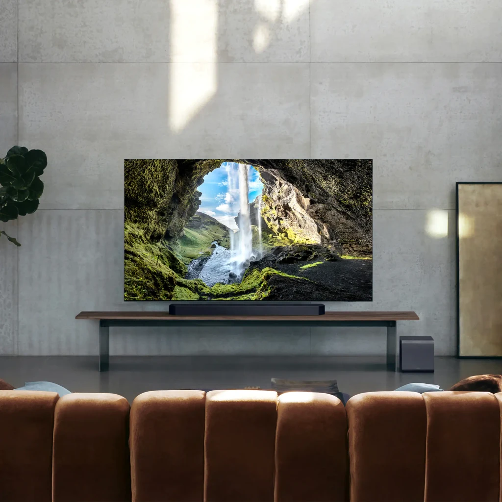 Samsung Barra de sonido HW-Q990F Dolby TrueHD negro, vista en salón: barra bajo TV con subwoofer lateral en mueble de madera
