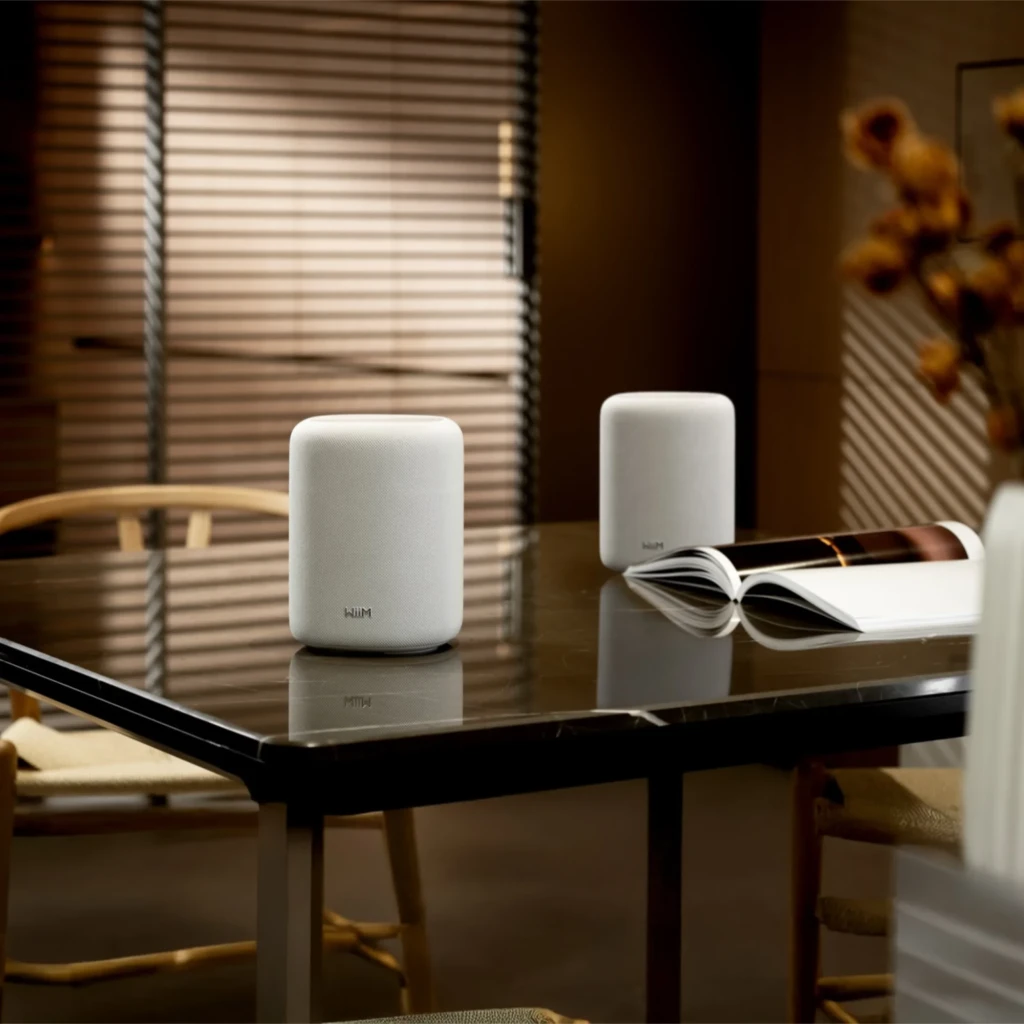 WiiM Sound Lite Twin Pack blanco, vista ambiental: dos altavoces sobre mesa negra con libro abierto y persianas de madera