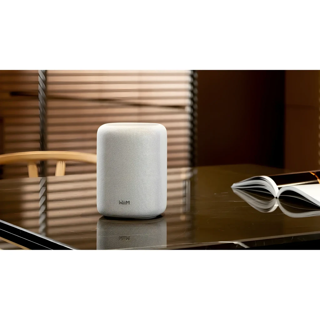 WiiM Sound Lite Twin Pack blanco, vista frontal en ambiente: altavoz sobre mesa oscura con libro abierto y persiana al fondo