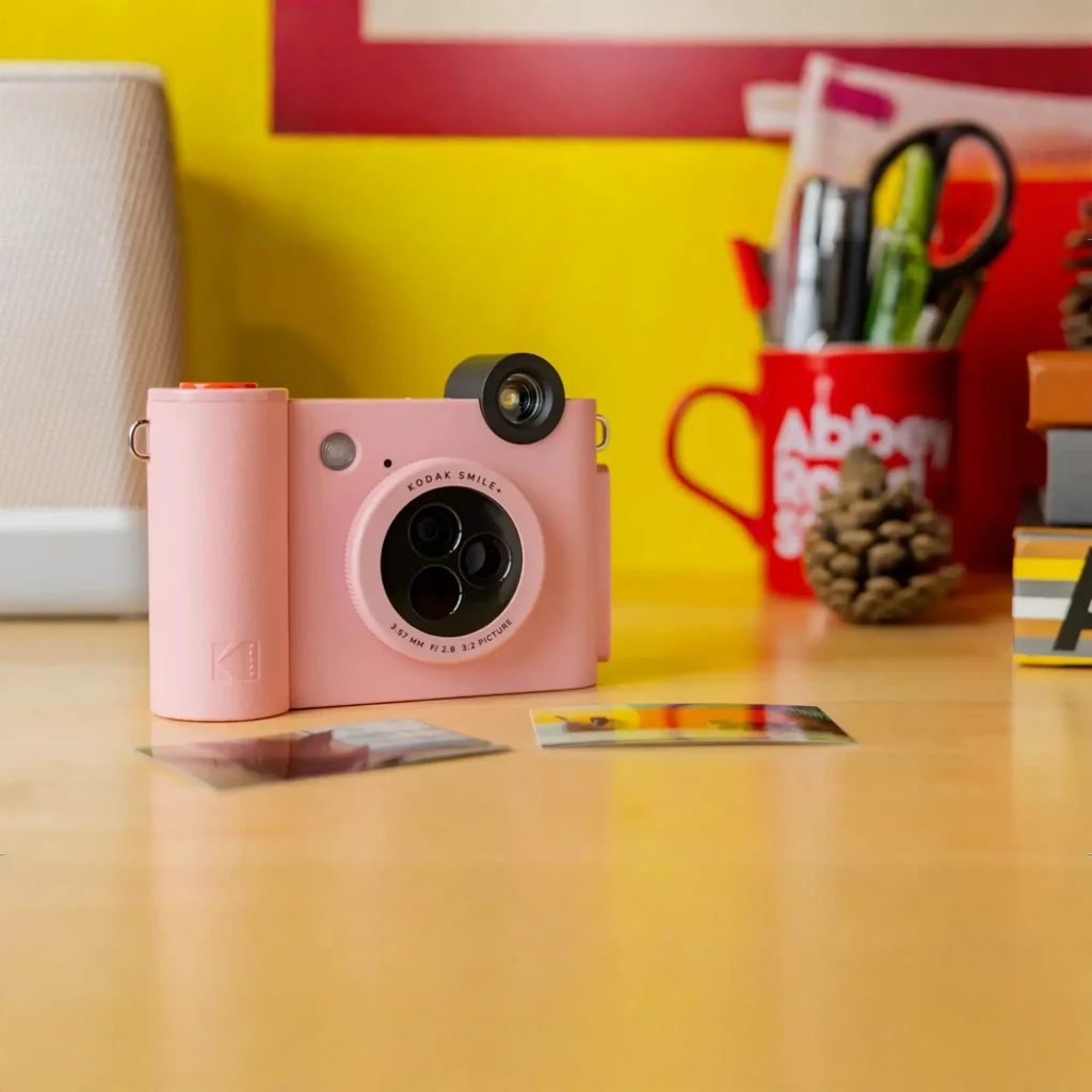 Kodak Instant Camera Smile+ 2x3 rosa, vista frontal en escritorio: módulo de cámaras, visor y fotos impresas delante