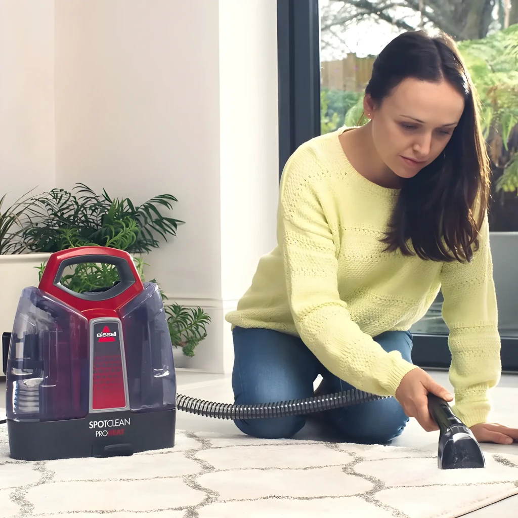 BISSELL SpotClean ProHeat 36988 Rojo Titanio, uso: mujer limpiando mancha en alfombra con manguera y accesorio