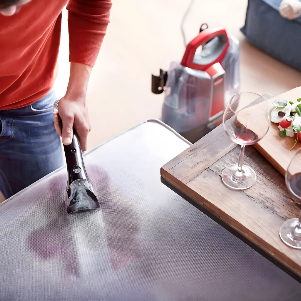 BISSELL SpotClean ProHeat 36988 Rojo Titanio, uso: persona limpiando mancha de vino en tapizado con accesorio