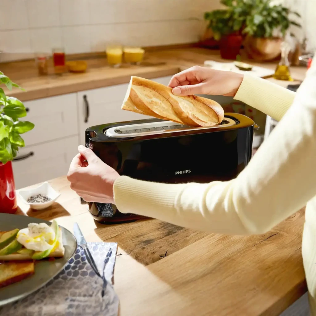 Philips Tostadora HD2590/90 Daily Collection Negro, uso: manos introduciendo baguette en ranura larga sobre encimera de