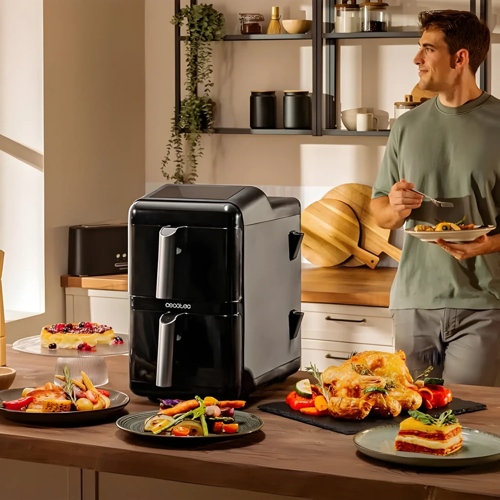 Cecotec Cecofry DuoLevel 12000 Window 12L Negro, escena cocina: freidora negra rodeada de platos cocinados y hombre al fondo