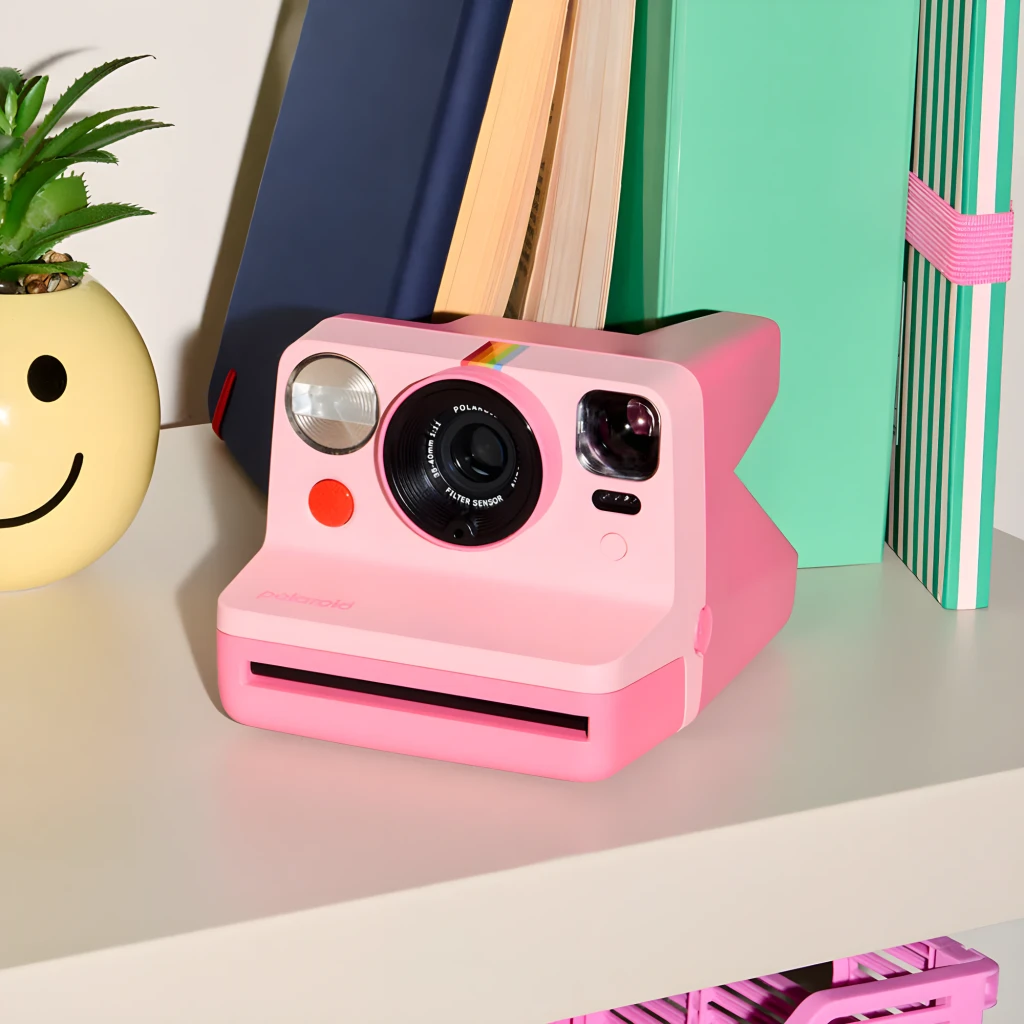 Polaroid Now Generation 3 Rosa, vista frontal en estantería: objetivo, flash, arcoíris y ranura de fotos visibles