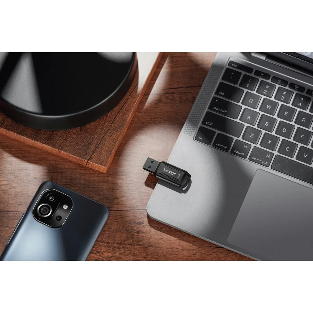 Lexar JumpDrive M400 64GB negro, vista cenital: conectada a laptop sobre mesa de madera junto a smartphone