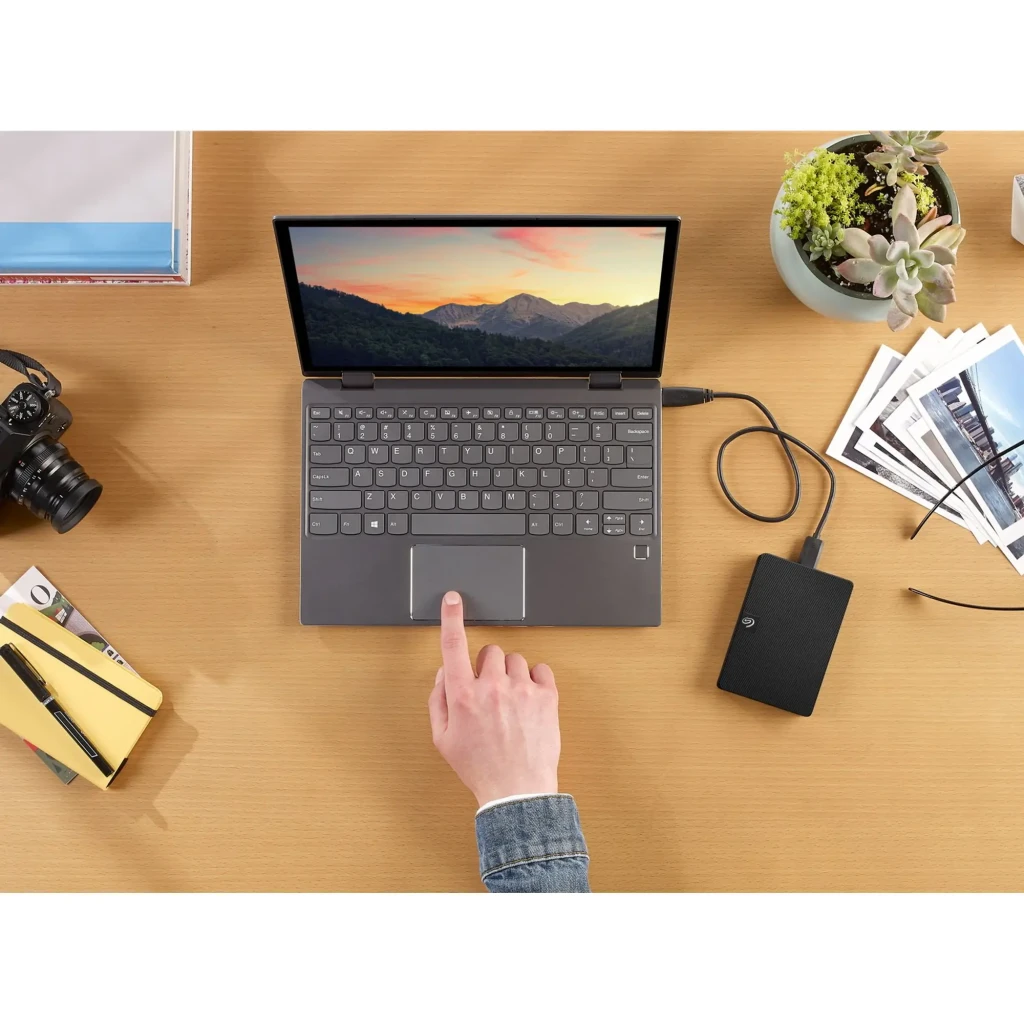 Seagate Expansion STKN1000400 1TB negro, vista cenital: disco conectado por USB a laptop sobre escritorio de madera