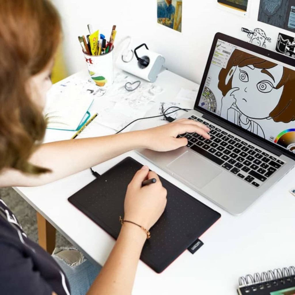 Tablette graphique Wacom One by Medium Noir avec stylet sans pile, surface noire à points, bords rouges, connectée en USB à un ordinateur portable pour