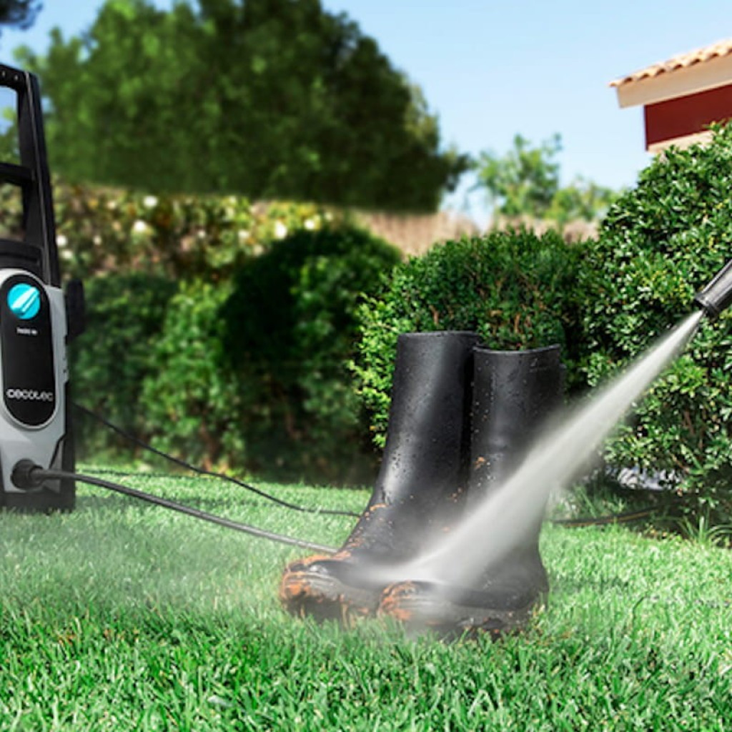 Cecotec HidroBoost 1400 EasyMove limpiando botas con chorro a presión; lanza en acción, manguera conectada y equipo compacto con ruedas y asa en jardín