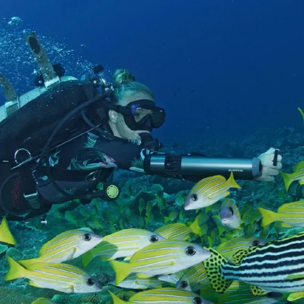 Waydoo Subnado Scooter subacuático ultra compacto sujetado al antebrazo, cuerpo cilíndrico gris con correas negras, propulsión potente en buceo entre peces