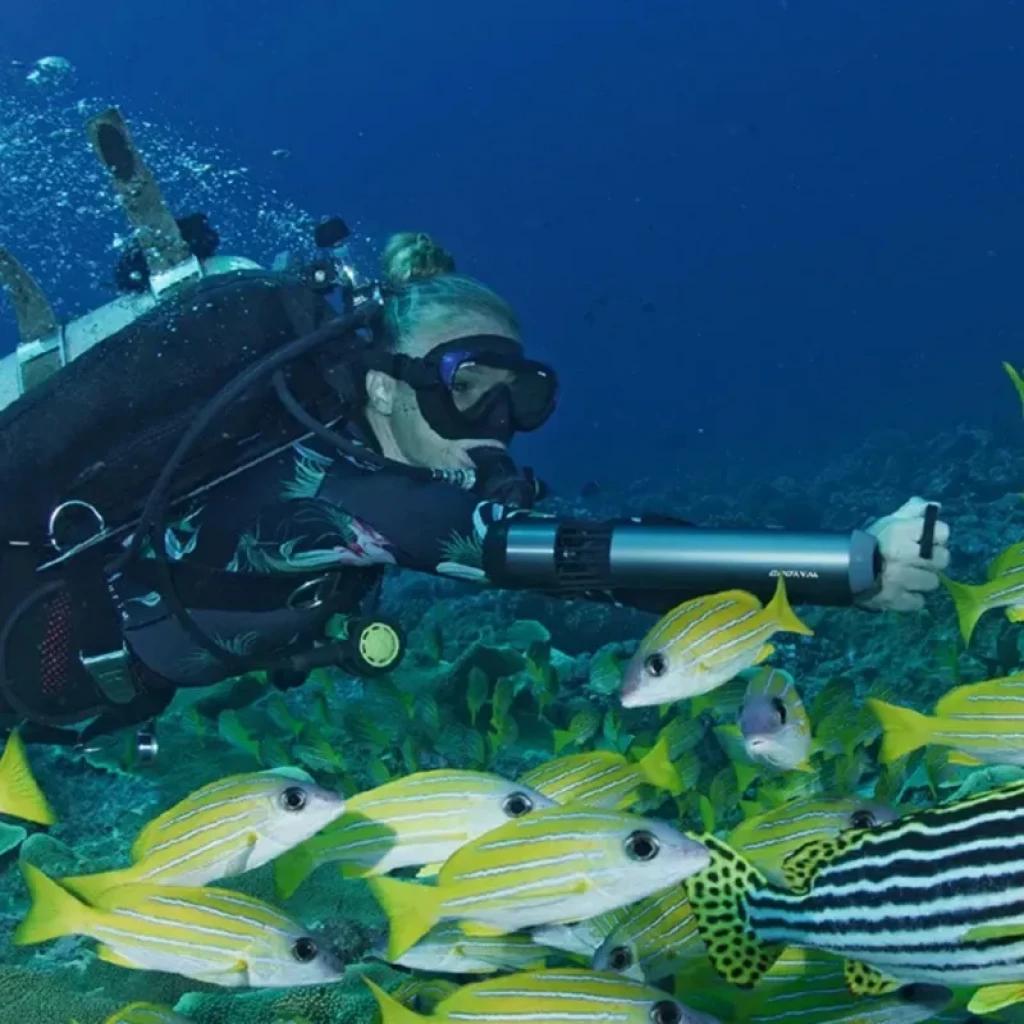 Waydoo Subnado Scooter subacuático ultra compacto sujetado al antebrazo, cuerpo cilíndrico gris con correas negras, propulsión potente en buceo entre peces