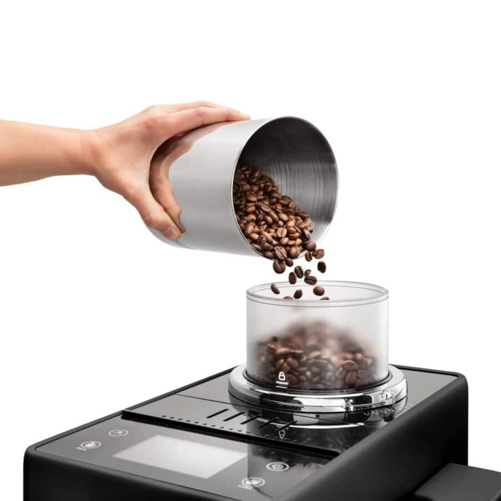 Depósito Bean Switch translúcido sendo abastecido com grãos de café, acoplado ao topo da DeLonghi Rivelia EXAM440.35.B com ecrã tátil e painéis pretos