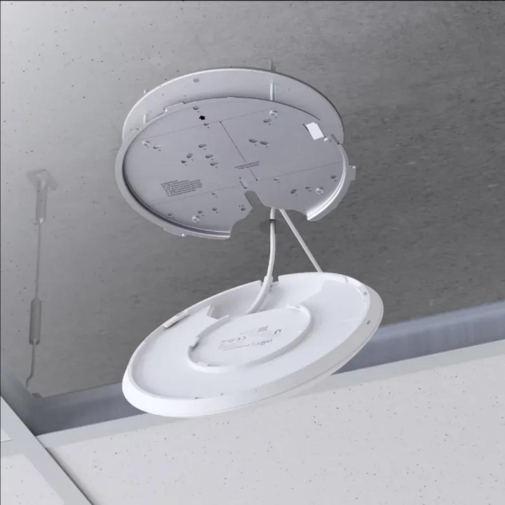 Point d'accès Ubiquiti U6 Enterprise monté au plafond avec plaque circulaire et câbles apparents, design blanc minimaliste pour installation PoE WiFi 6E