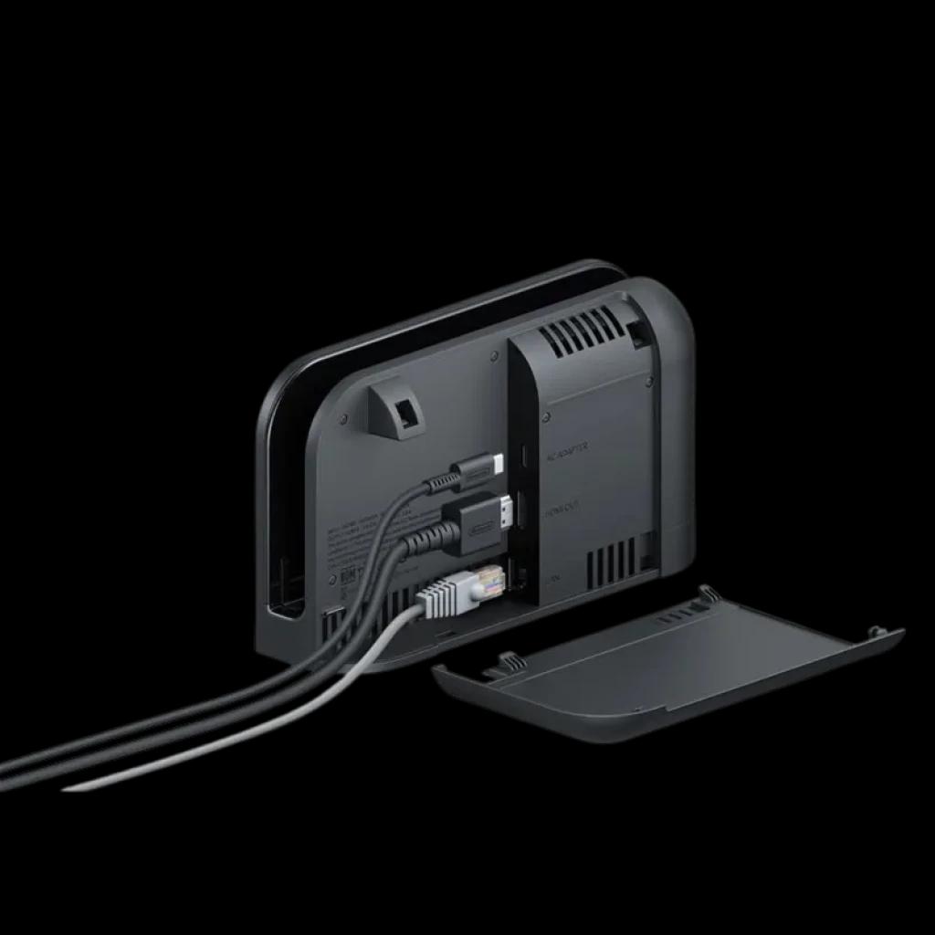 Base Nintendo Switch 2 vista traseira com tampa removida, três cabos conectados, portas HDMI e USB visíveis, design preto fosco com grelhas de ventilação