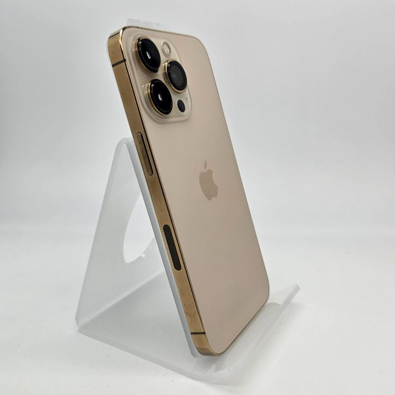 iPhone 13 Pro 256GB oro renovado en excelente estado, acabado dorado mate, bordes brillantes, triple cámara con lentes grandes, apoyado en base acrílica