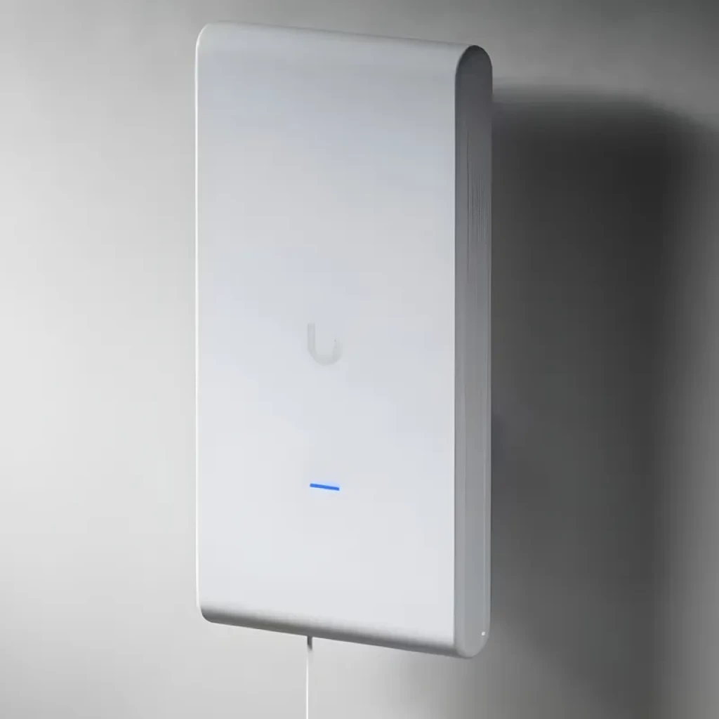 Ubiquiti U6 Mesh Pro Blanco montado en pared, diseño rectangular minimalista, LED azul frontal, carcasa lisa, ventilación lateral y cable inferior visible