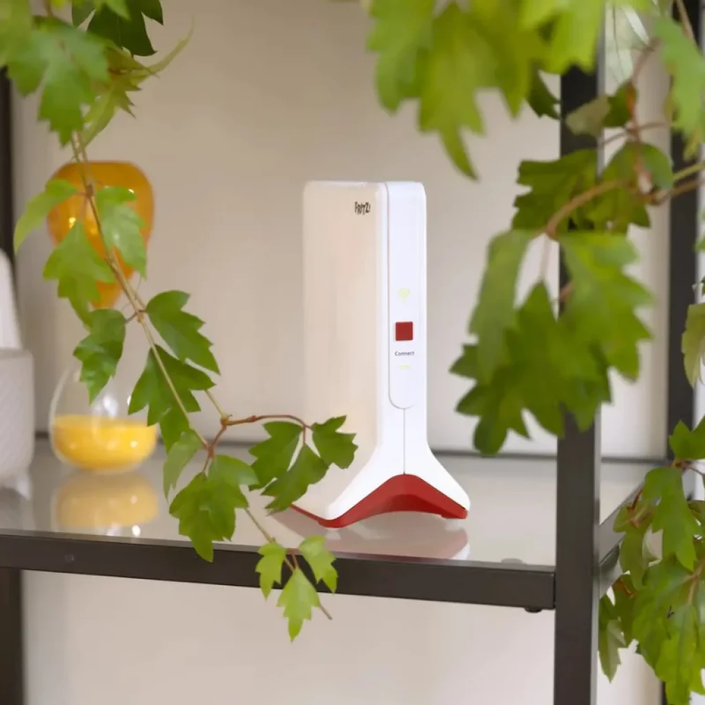 Repetidor FRITZ!Repeater 6000 WiFi 6 tribanda en color blanco con base roja, luz LED de estado y botón Connect, diseño vertical sobre estante interior