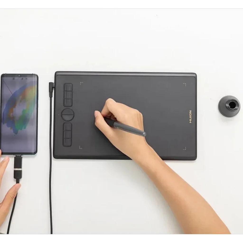 Huion H580X com 8 teclas programáveis, área preta ampla, caneta sem bateria em uso, conexão USB a smartphone e suporte para ponteiras ao lado