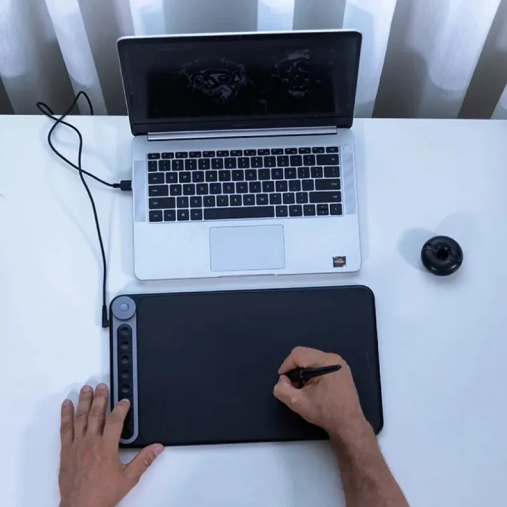 Huion Q620M com área ampla, 8 botões e dial lateral; caneta sem bateria em uso com laptop via USB-C; suporte a conexão sem fios 2,4 GHz