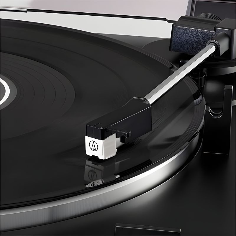 Audio Technica AT-LP60X Tocadiscos con brazo recto y cápsula AT, aguja sobre vinilo en plato giratorio brillante, detalle cercano de la cápsula y surcos